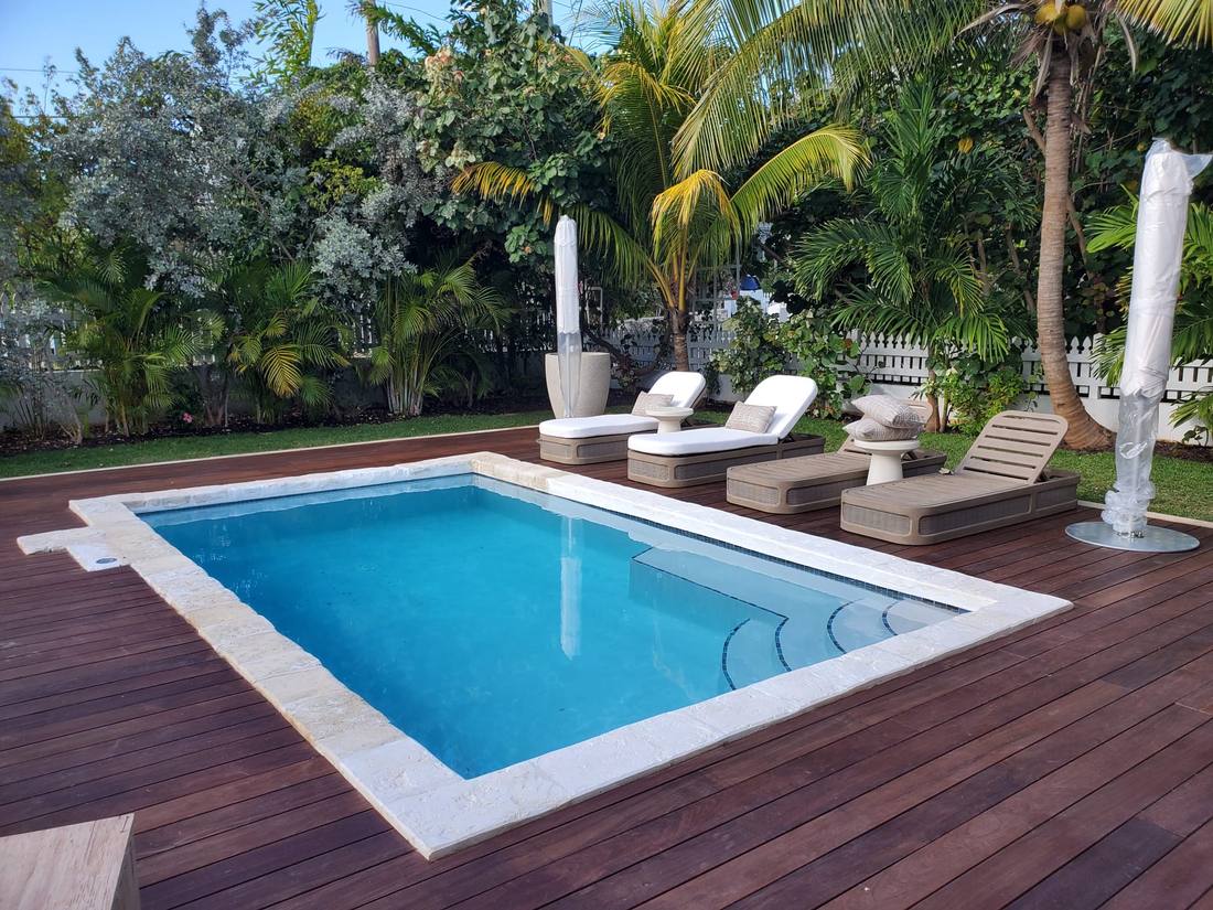 Swimming pool set into a hardwood deck with loungers and palms.