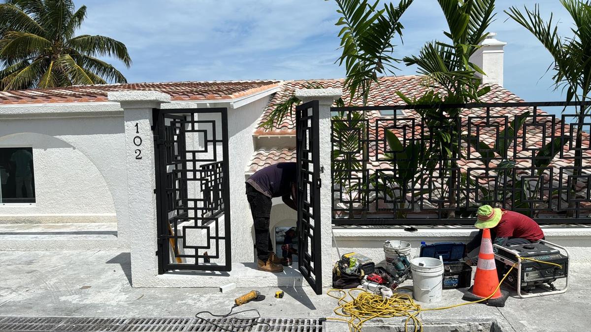 Custom fabricated steel gate with a geometric fretwork pattern being installed at a property entrance.