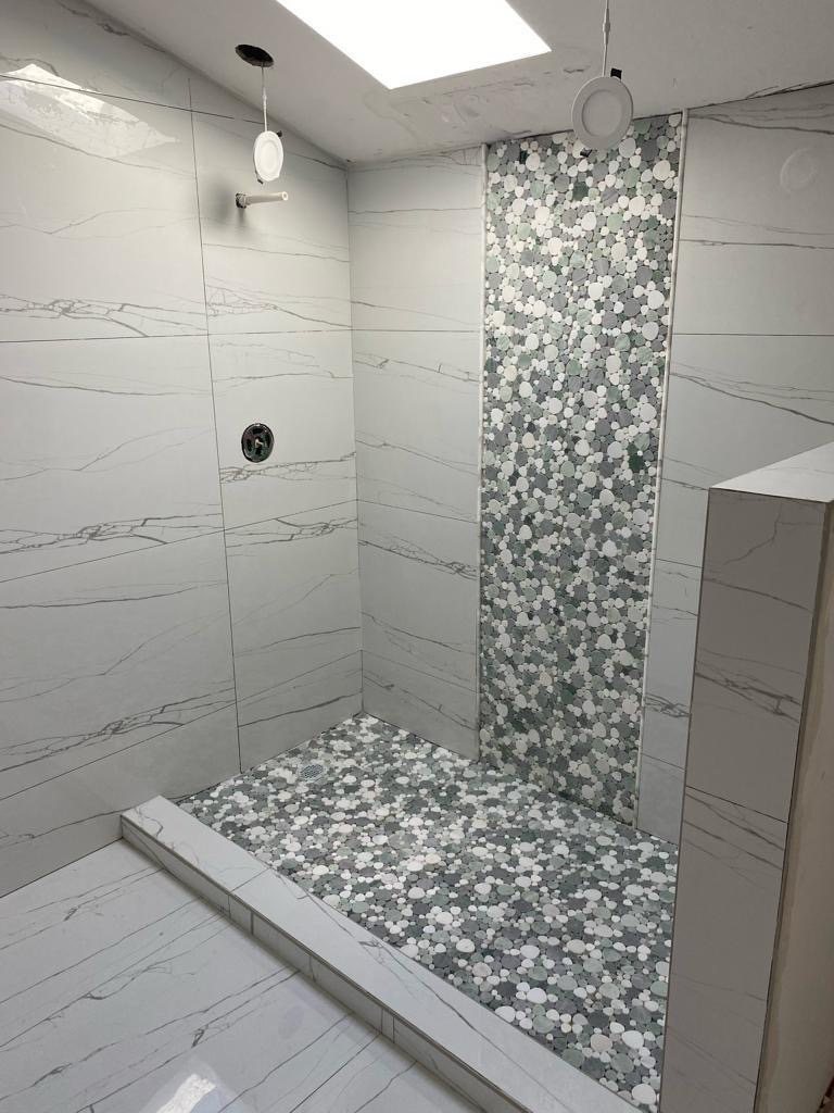 Marble tile shower with pebble mosaic floor and skylight above.