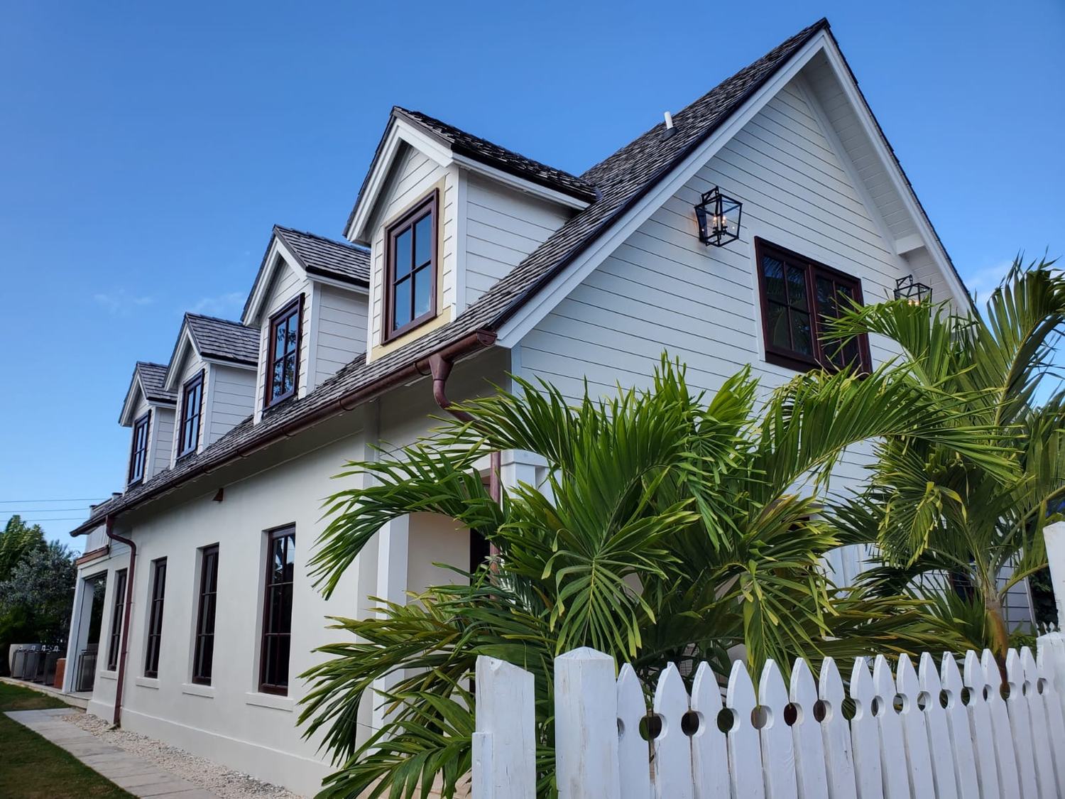 Two storey home at Old Fort Bay at dusk, with dormer windows, mahogany trim and palms.