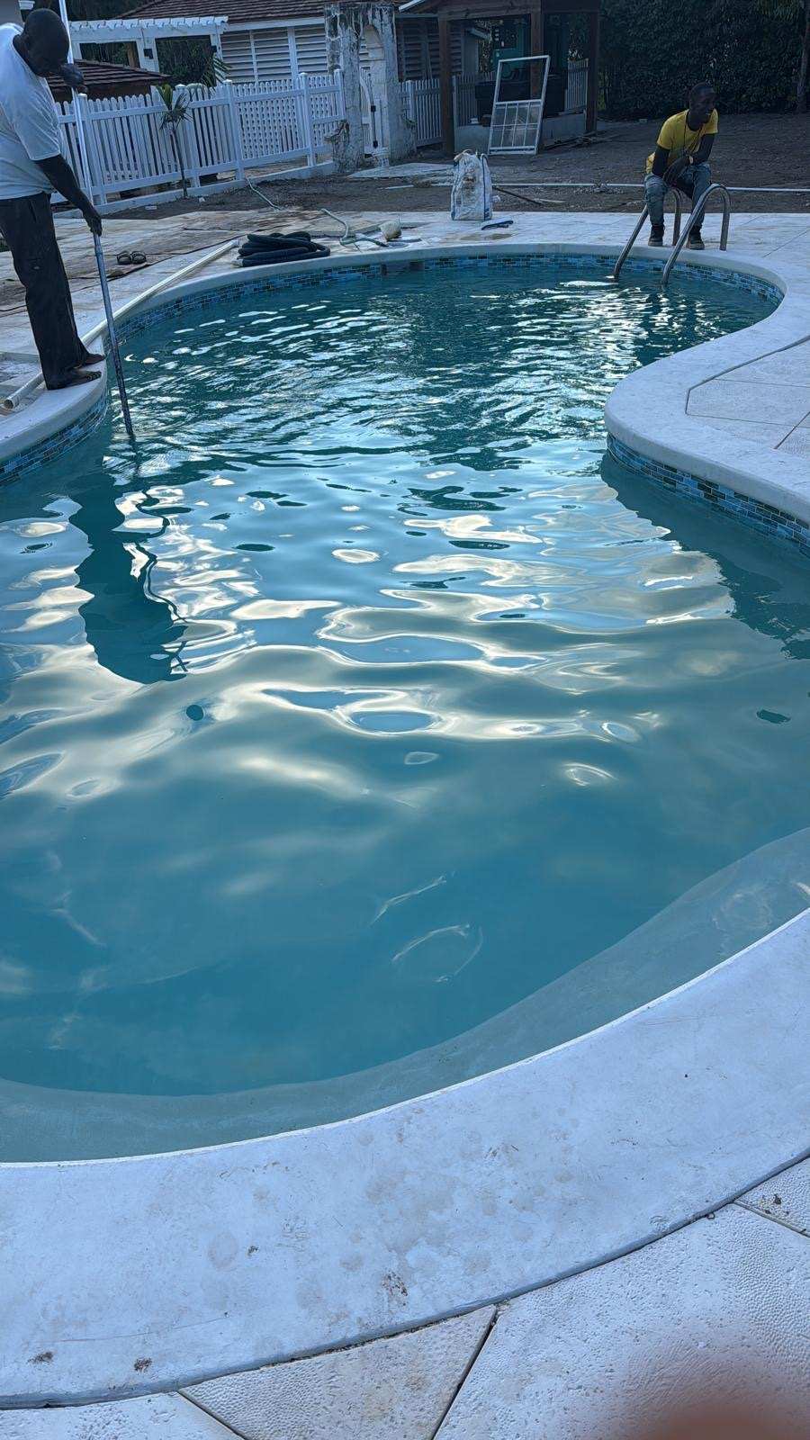 Crew finishing a newly filled swimming pool with mosaic tile edge.