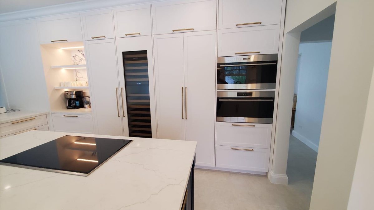 Kitchen with full height white cabinetry, brass handles, integrated wine store and marble island.