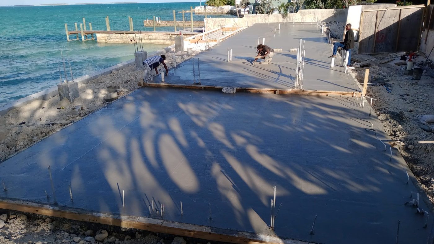 Crew finishing a poured concrete slab at the seawall with the ocean beyond.