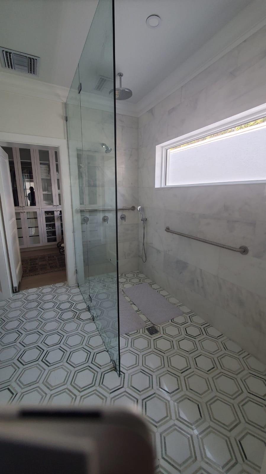 Marble lined walk in shower with a patterned hexagonal tile floor.