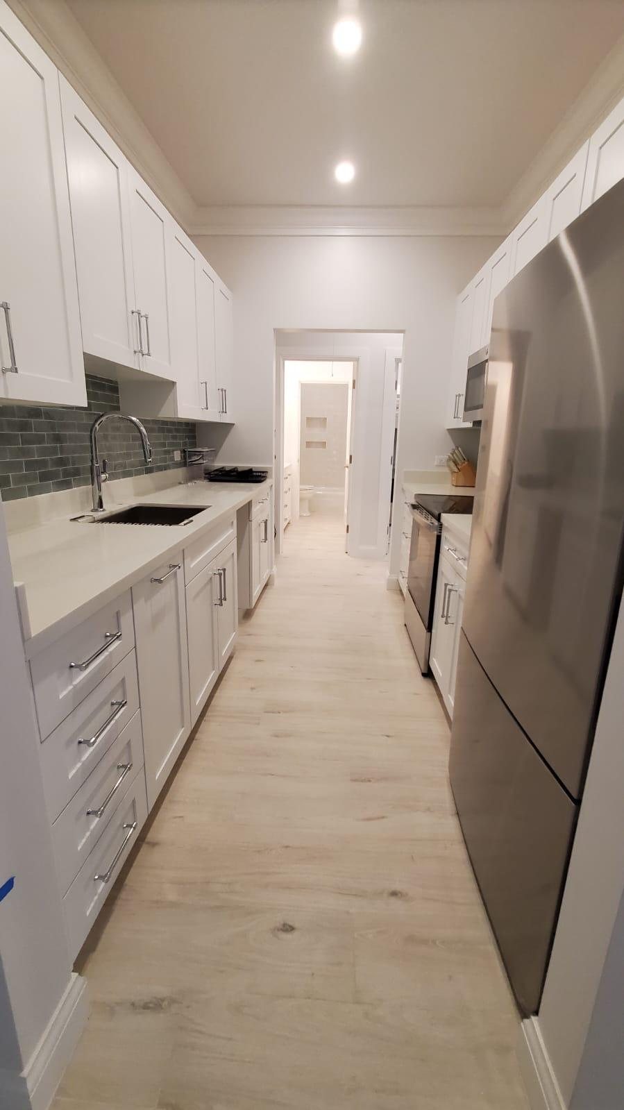 Galley kitchen with white shaker cabinets, green tile backsplash and stone counters.