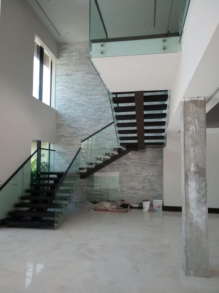 Floating timber staircase with glass balustrade against a stacked stone wall.