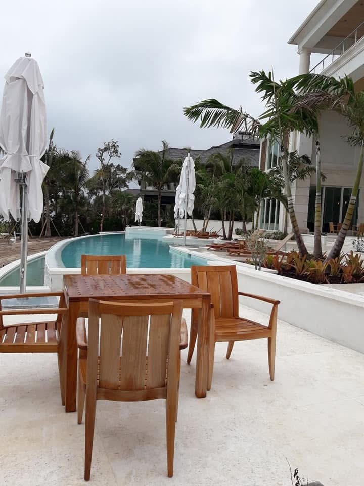 Curved pool edge and travertine terrace with teak furniture and planting.