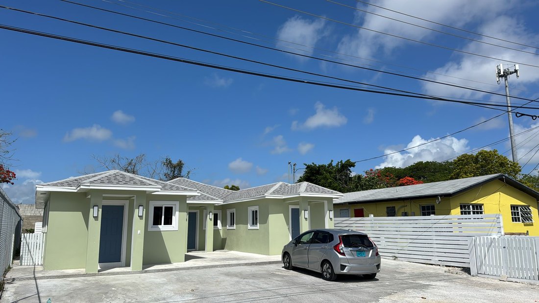 Row of completed apartment units seen from the street with a paved forecourt.