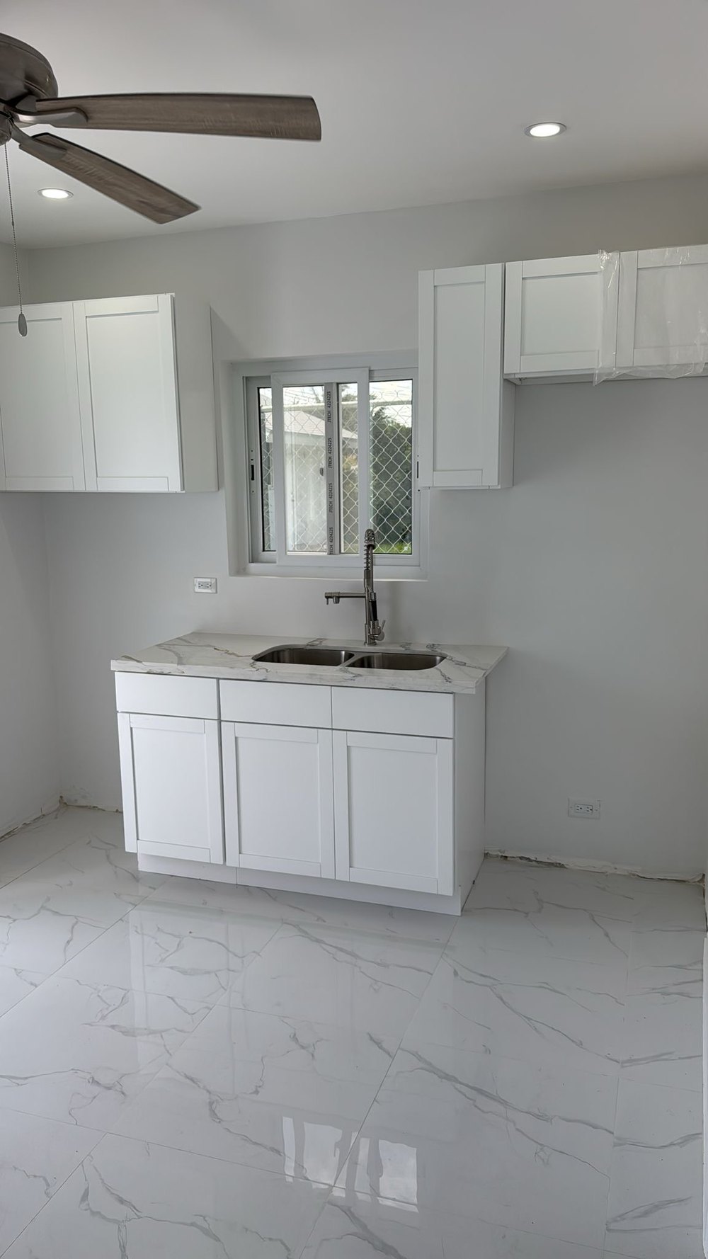 Kitchen with white shaker cabinets, marble effect counter and stainless sink.