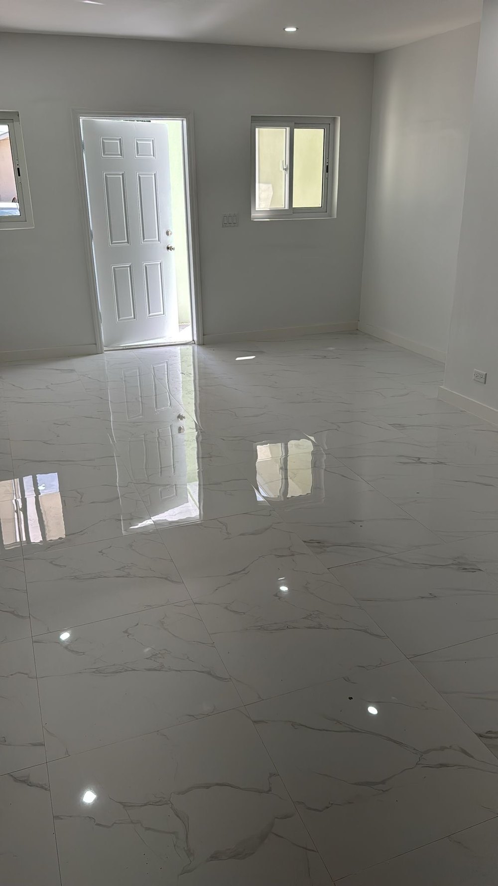 Living area with front door and window, finished in polished floor tiling.