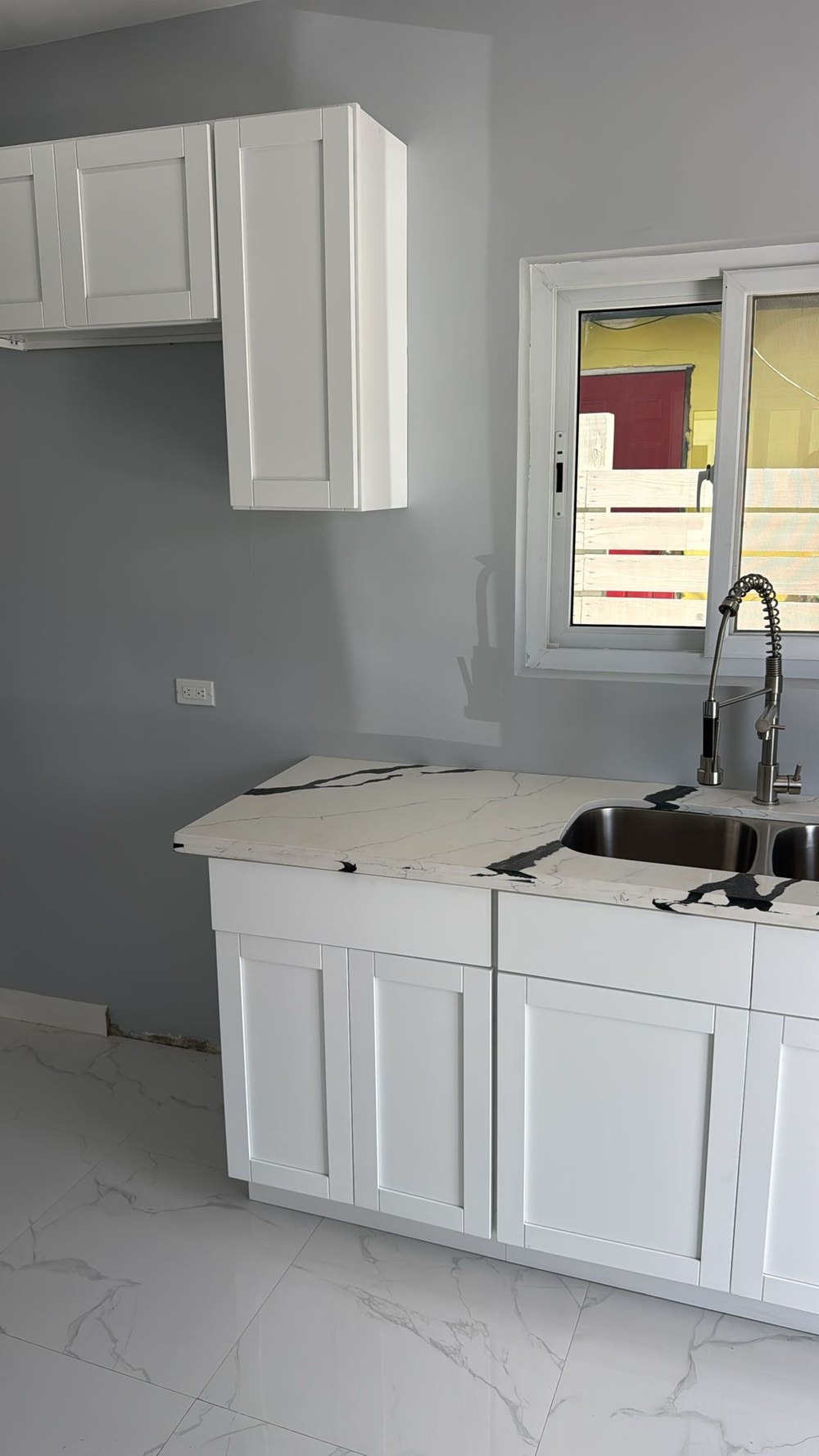 Kitchen run with white cabinets and a veined stone counter against a grey wall.