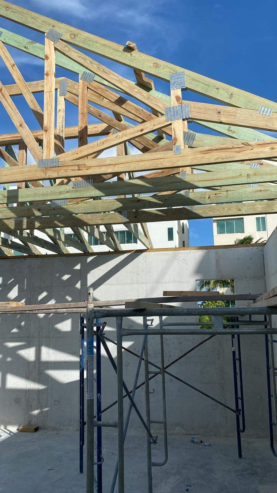 Timber roof trusses in place against a clear sky above concrete walls.